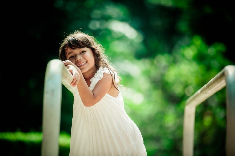 Children Singapore Photoshoot Outdoor smiling girl in white dress leaning on exercise bar