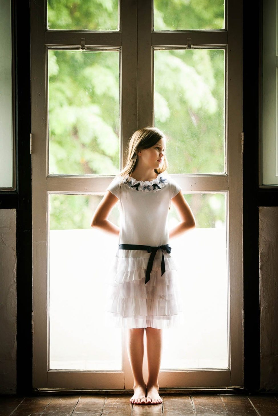 Kids Singapore Photography Natural portrait of girl in white dress with black ribbon leaning against door