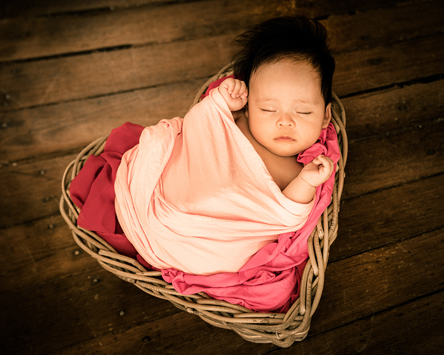 100 days old baby girl swaddled and sleeping peacefully in a heart-shape basket in White Room Studio