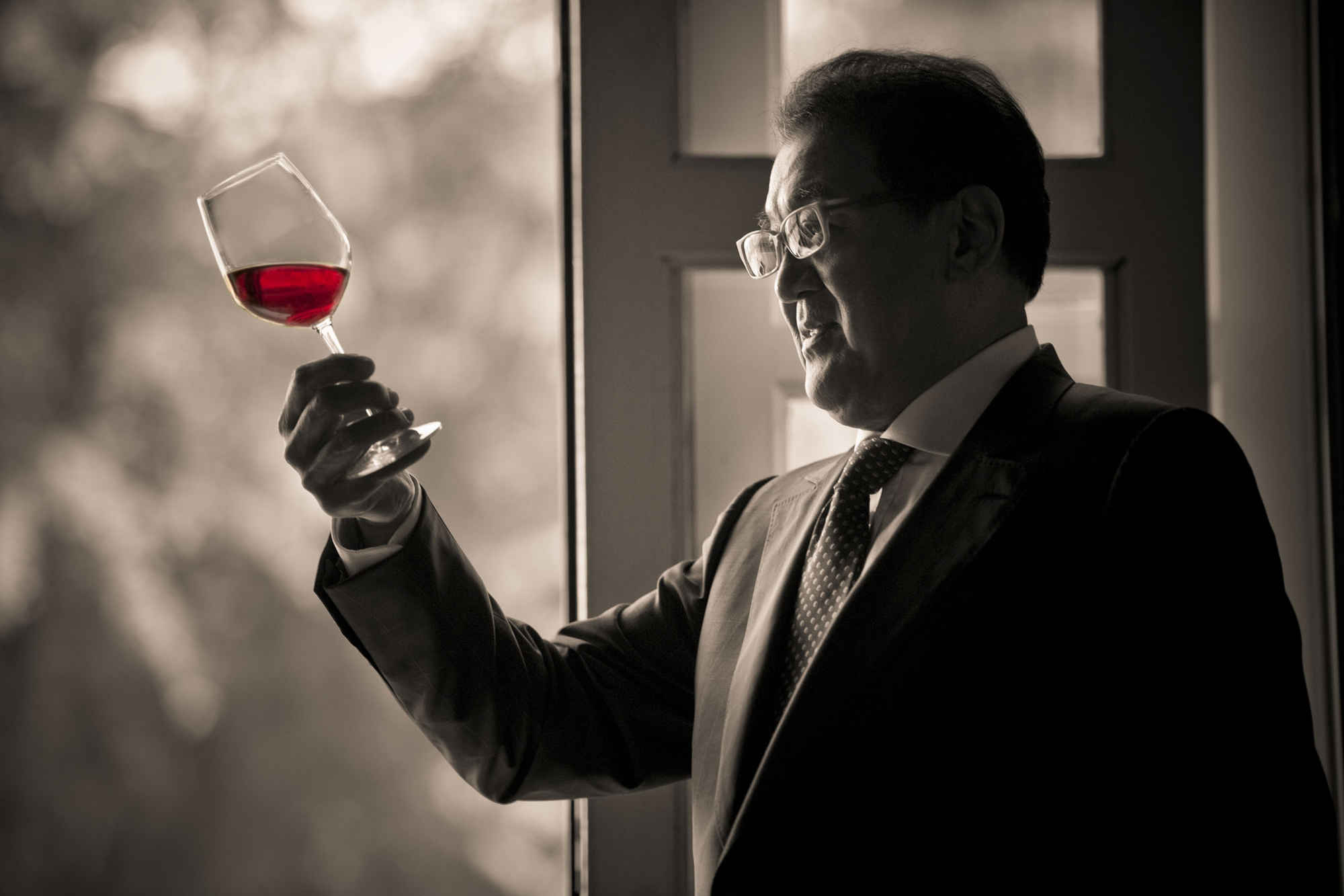 Black and white photo man in suit holding a glass of red wine balcony nature scenery during a professional personal branding photoshoot in Singapore Credit: White Room Studio Pte Ltd