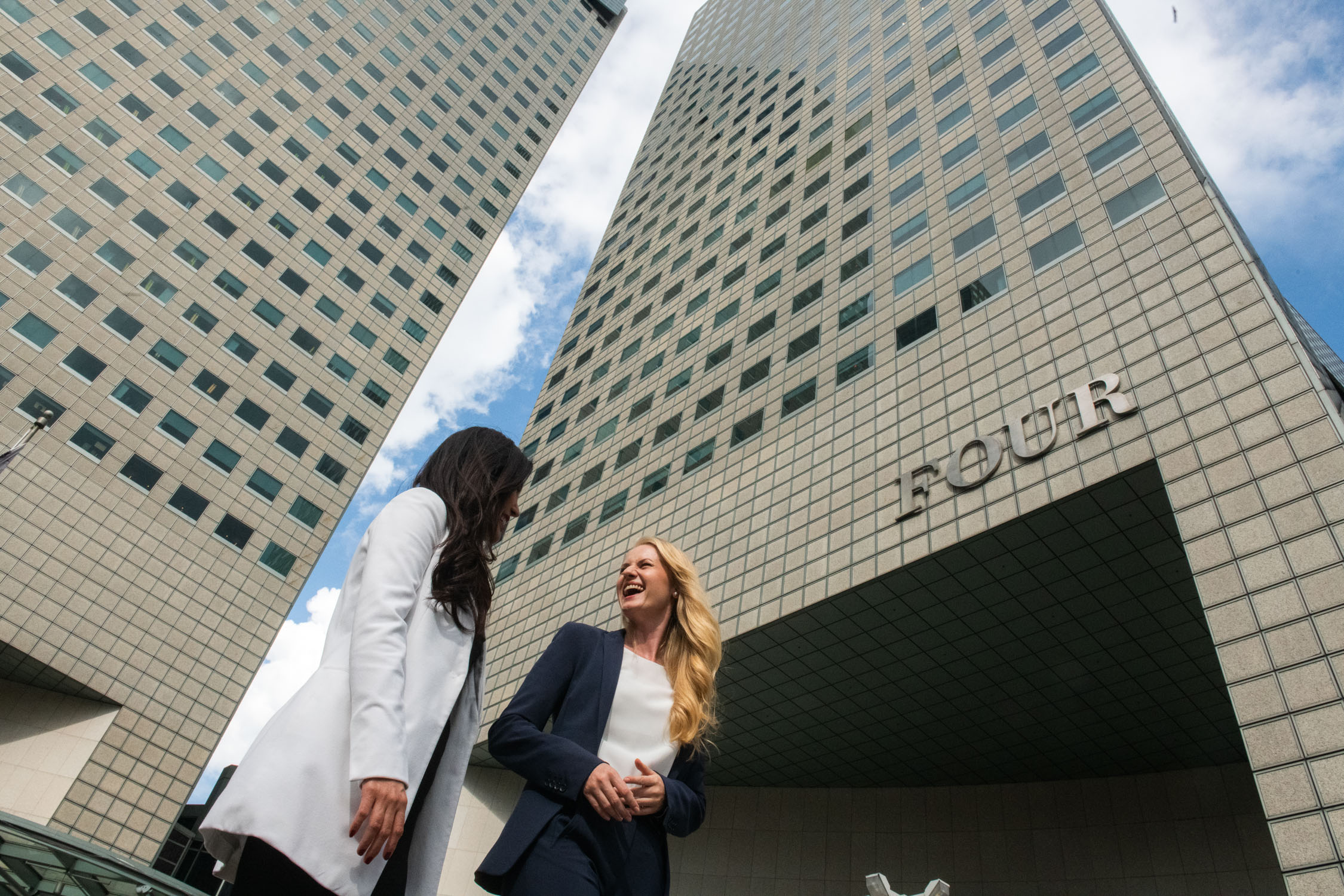 Two women in formal corporate attire walking and talking together outside an office building