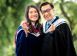 Father and daughter in graduation gowns, smiling and showing finger hearts