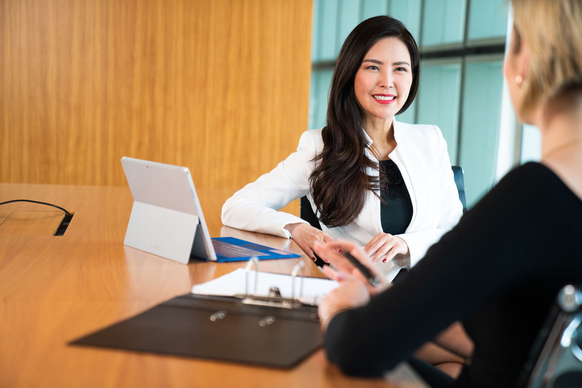 Asian woman in a white blazer smiling at her colleague in an office setting