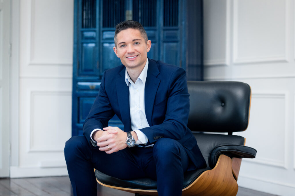 Professional_headshots_07 Caucasian man in a blue formal corporate suit sitting down on a black leather armchair posing for his headshot