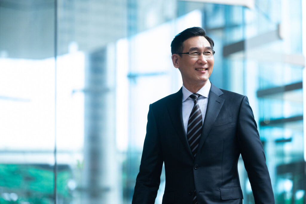 Asian man in a formal business suit walking outdoors in Singapore, outside office building. Credit: White Room Studio