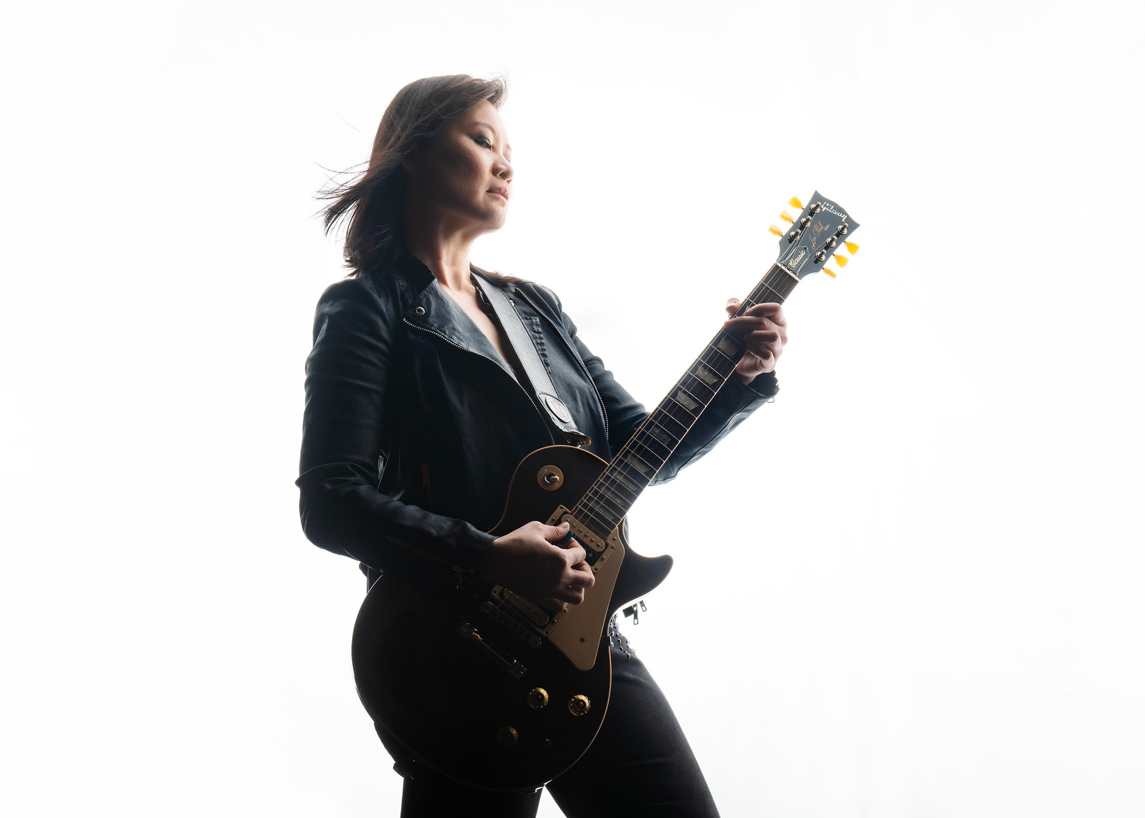 Woman plays an electric guitar against a white studio backdrop