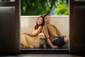A couple sitting on a balcony with their pet dog (maltipoo)
