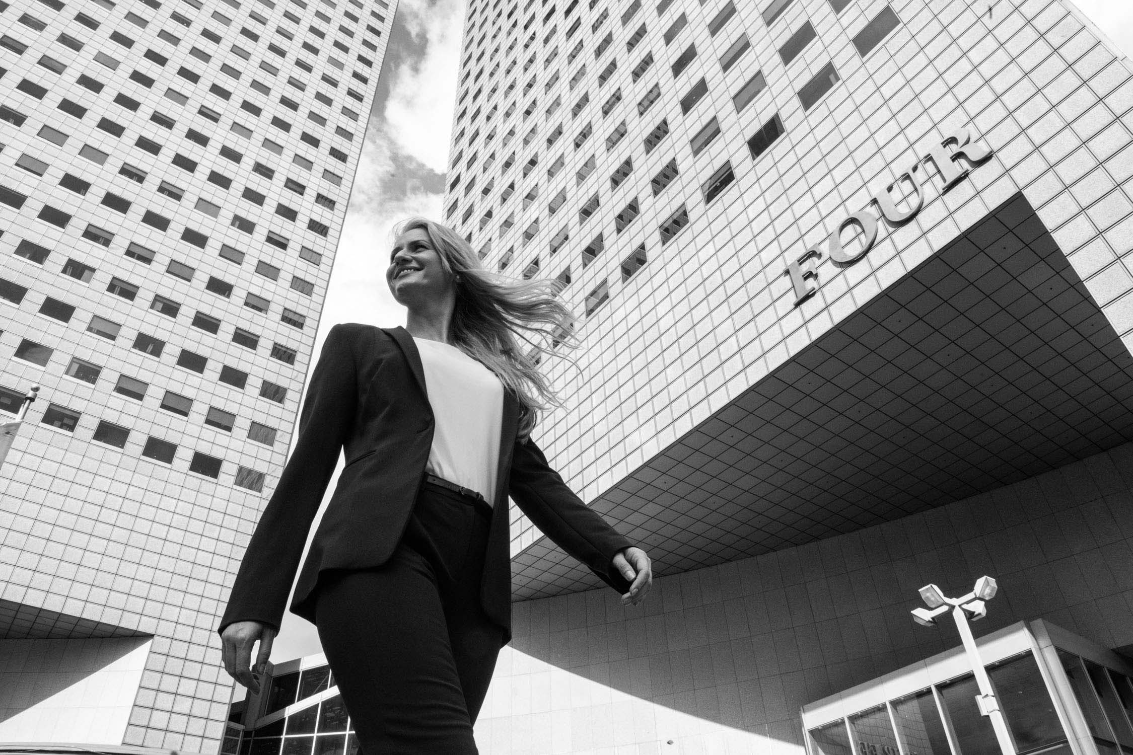 Black and white photo of a woman in a formal suit walking across office buildings during a corporate outdoor photoshoot in Singapore Credit: White Room Studio