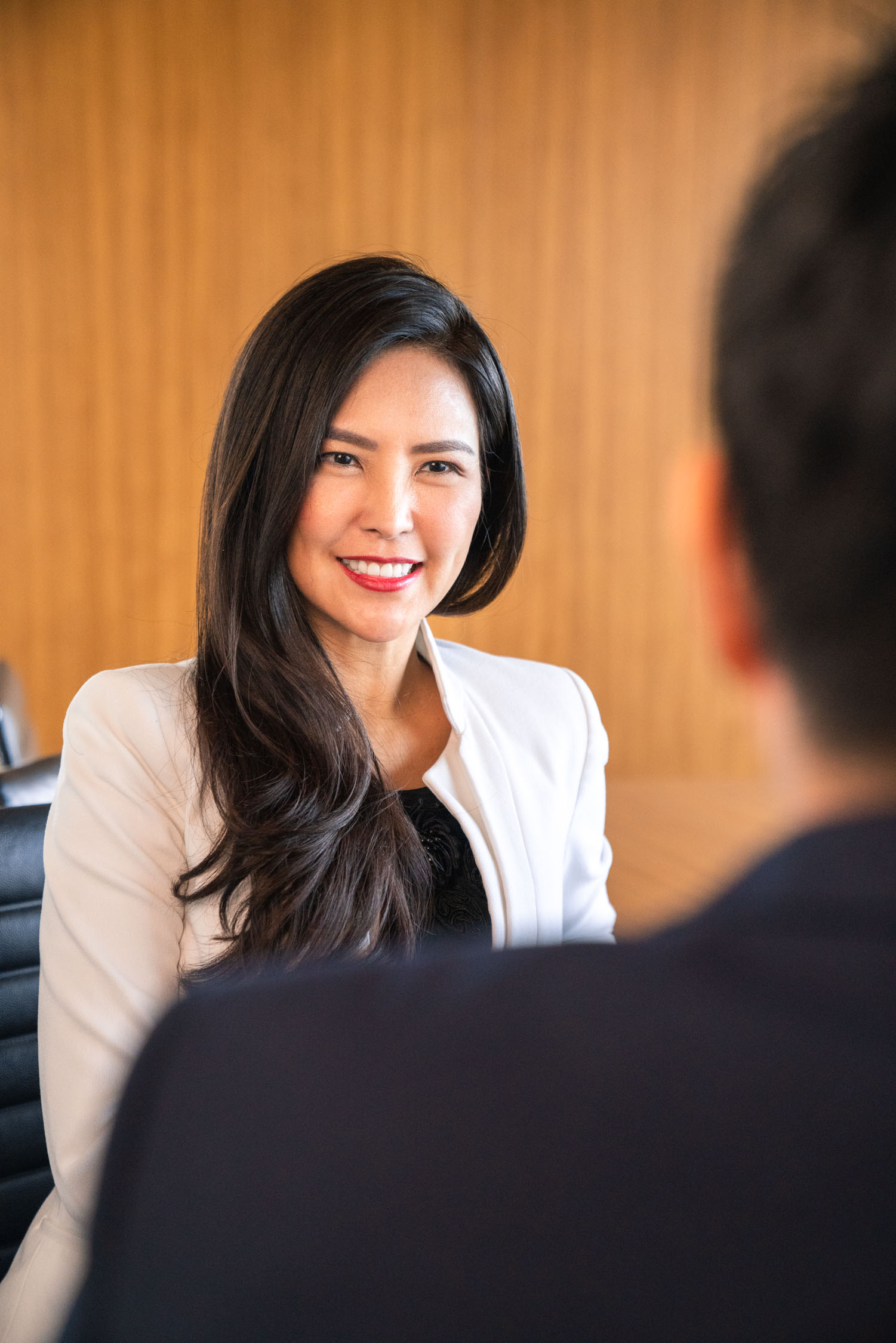 An Asian woman with long hair in a white blazer and black blouse smiling at client