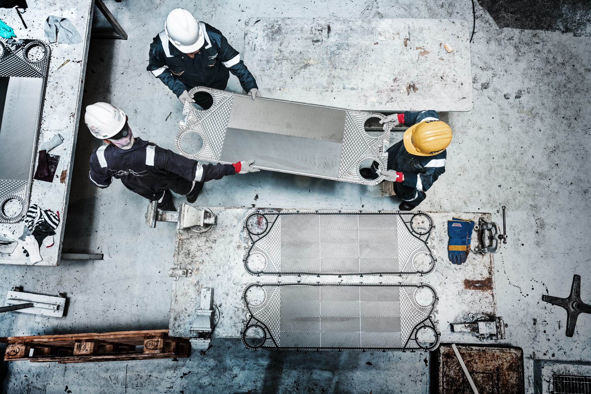 A top down photo of three male workers wearing hard hats lifting steel machinery during a professional outdoors photoshoot in Singapore