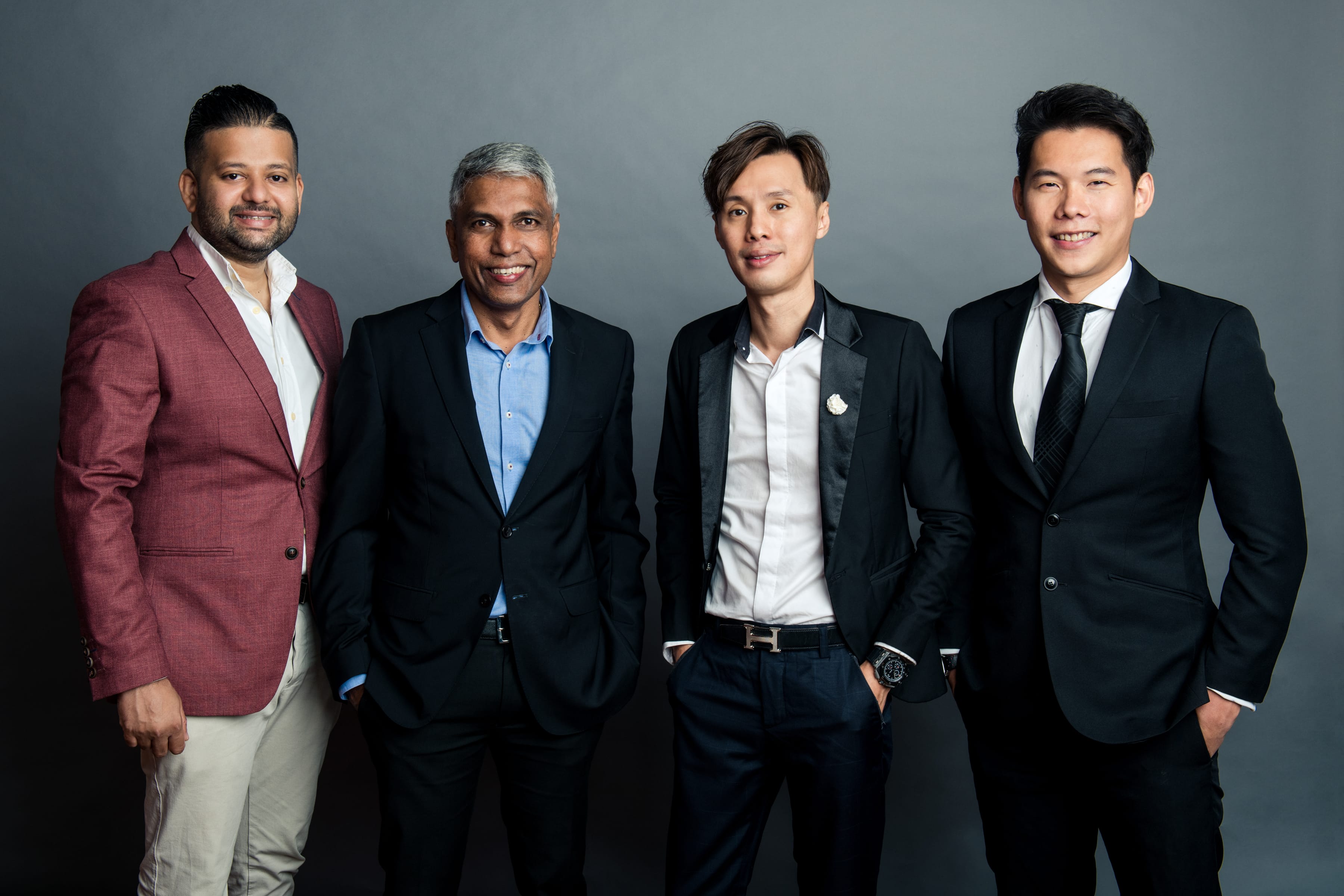 A group photo of four male corporate professionals in formal business suit standing against a grey studio background during a corporate photoshoot in Singapore Credit: White Room Studio