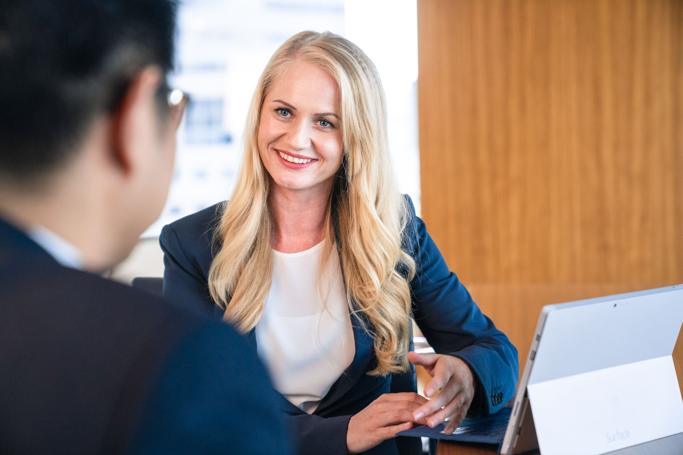 A woman with blonde long hair in a dark blue blazer and white blouse smiling at a client during a professional corporate photoshoot in Singapore