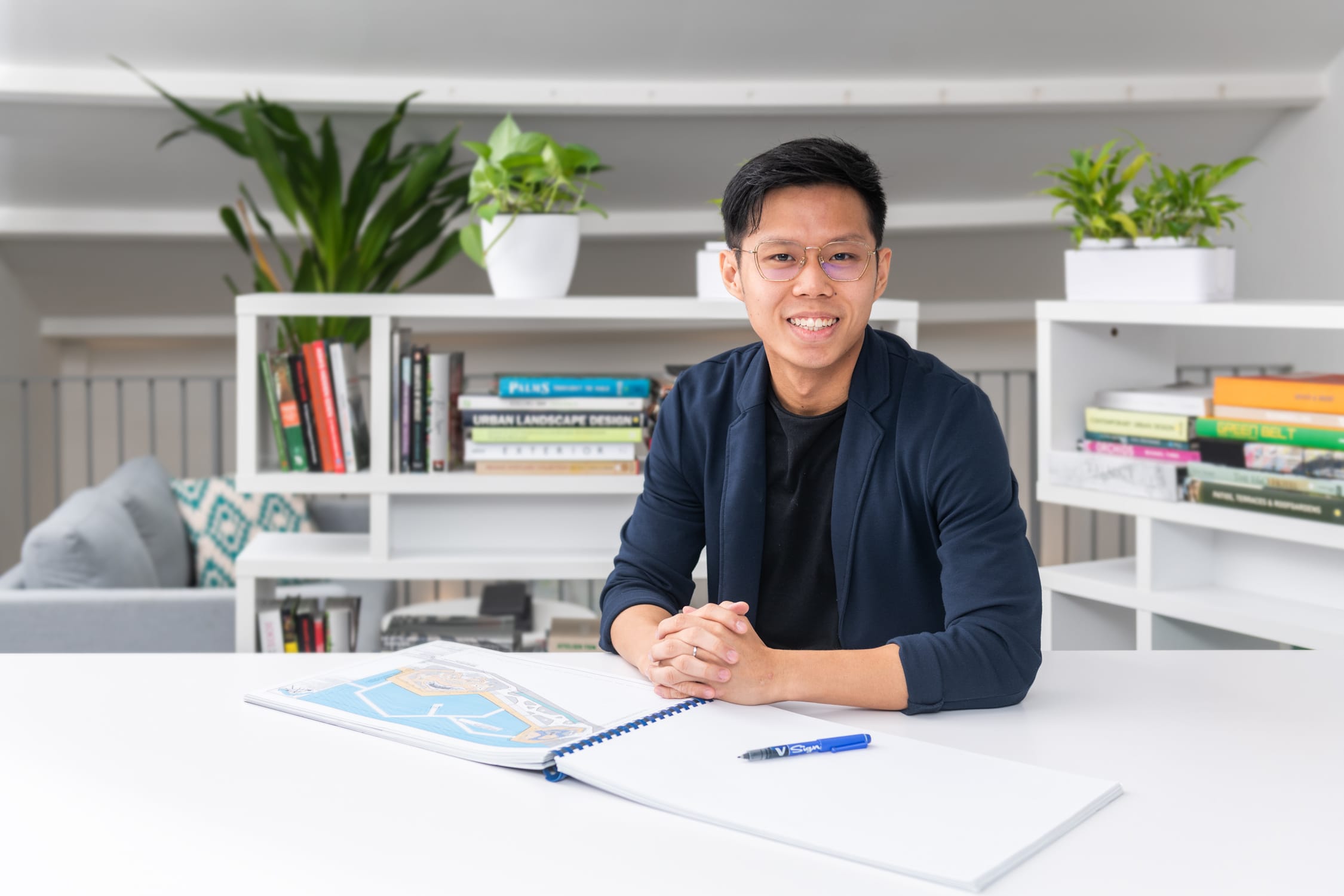 A man working on a project with a book in front of him in an office setting, smiling for his headshot during a corporate photoshoot in Singapore Credit: White Room Studio