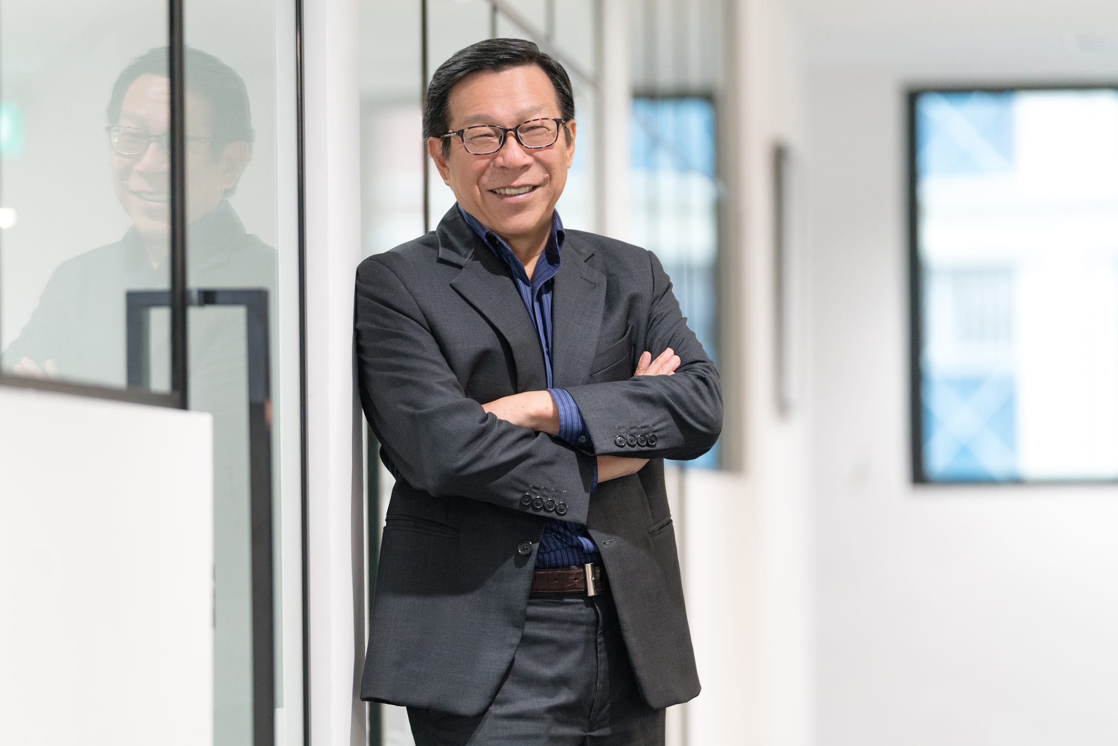 A man in a formal business suit poses for his headshot in an office setting, arms crossed during a corporate photoshoot in Singapore Credit: White Room Studio