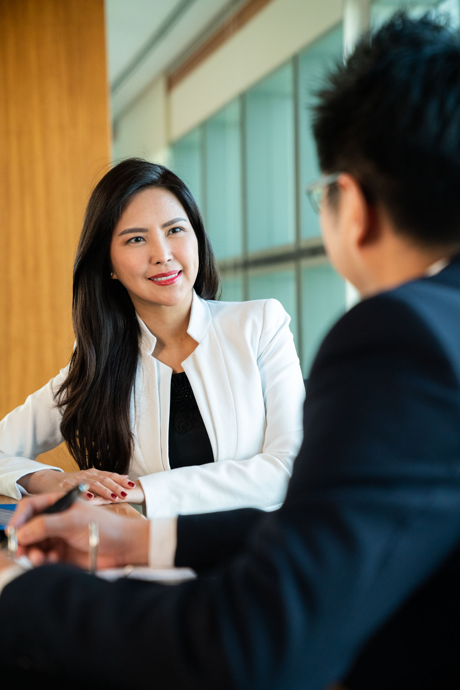 A woman with long hair in a white blazer and black blouse smiling at client during a professional corporate photoshoot in Singapore