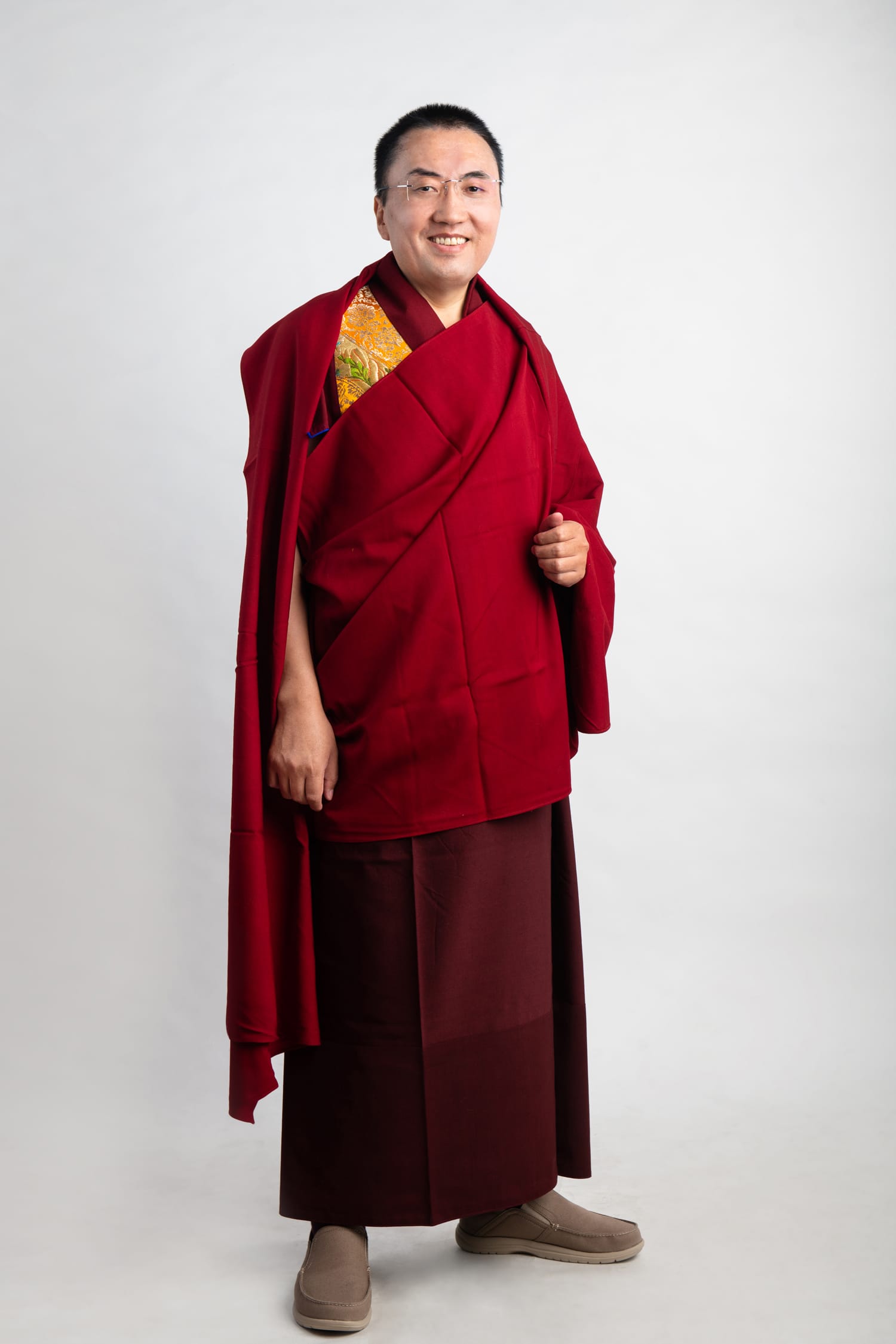 A monk (rinpoche) wearing red traditional robes poses for his headshot during a professional indoor photo shoot in Singapore