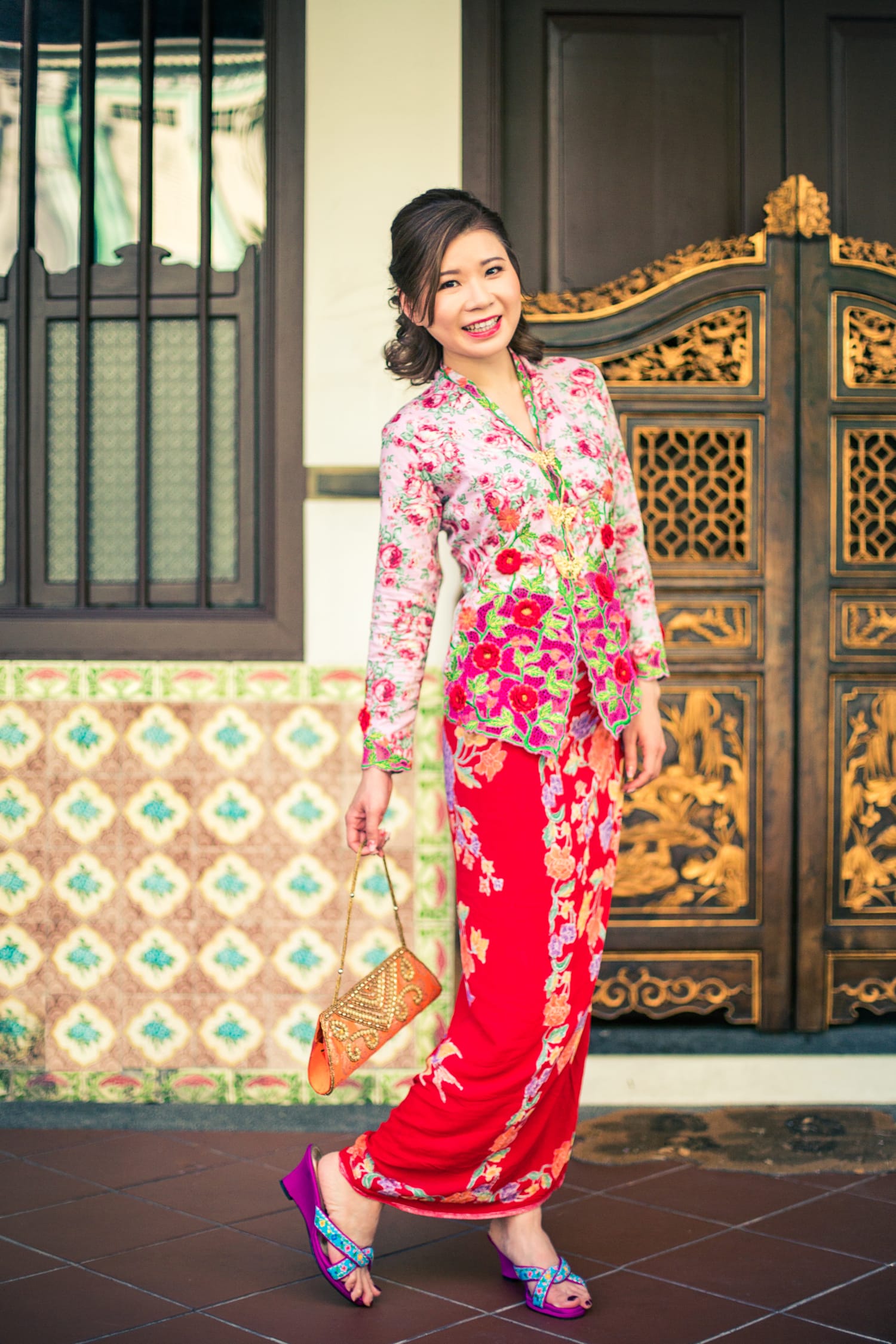 A woman in a traditional pink and red Peranakan costume poses outside a Peranakan museum during a professional indoor photo shoot in Singapore