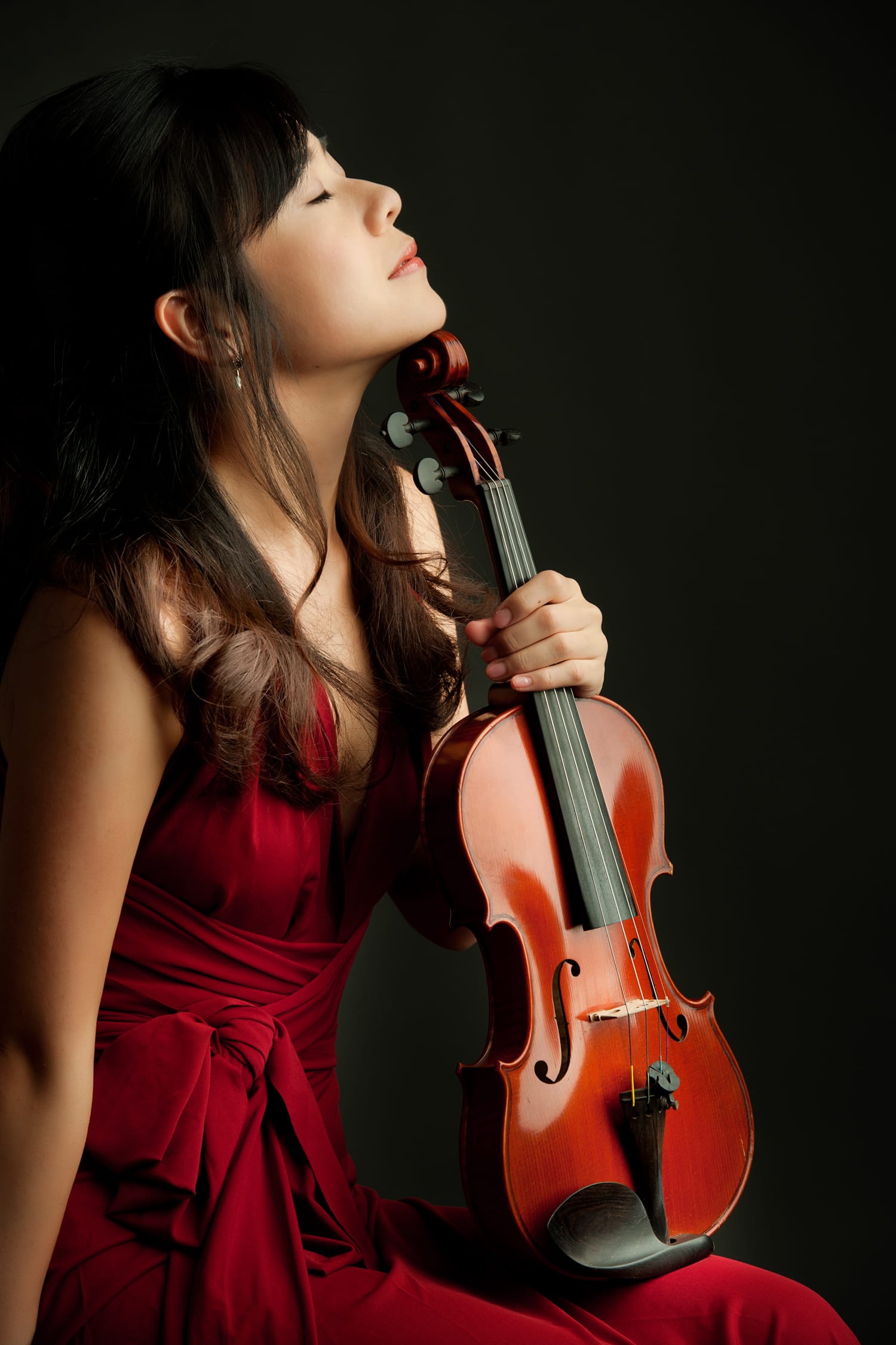 A woman in a pink dress poses with her violin during a professional indoor photo shoot in Singapore