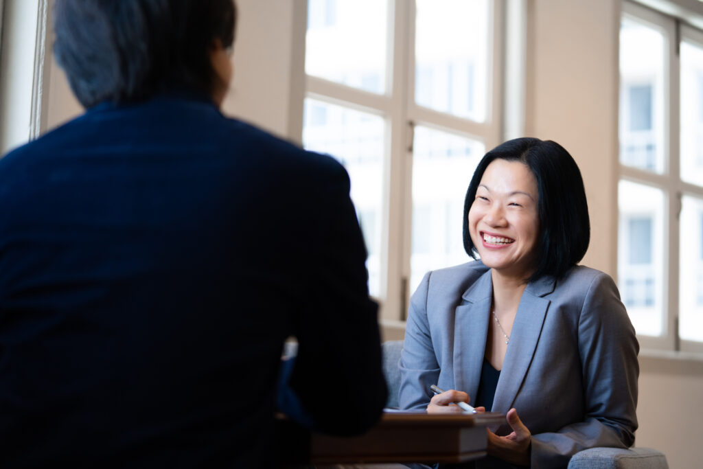 A woman in a grey blazer smiles at a man sitting across her during a professional corporate photoshoot in Singapore Credit: White Room Studio