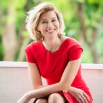 A woman in a red dress sitting on a wooden bench posing for her headshot during a professional corporate headshot photographed in natural light at White Room Studio, 219 River Valley Road Singapore