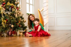 Mother and daughter hugging and smiling with Christmas tree and fairy lights decorations during Christmas family photoshoot in Singapore Credit: White Room Studio