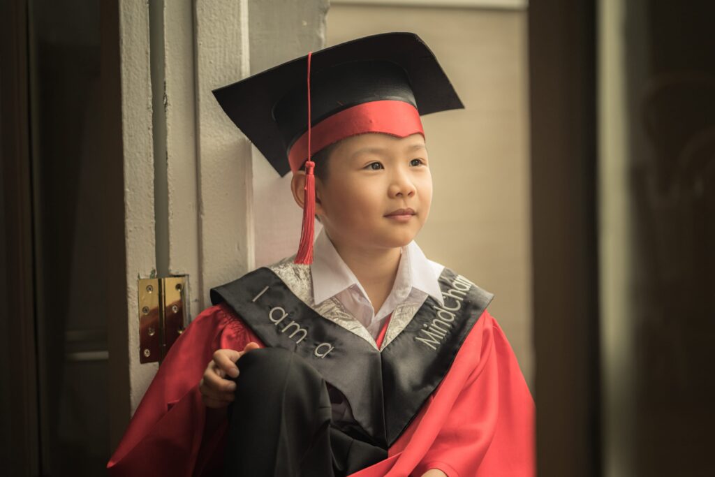 Young boy in Mindchamps red and black K2 kindergarten graduation gown and cap during K2 kindergarten graduation photoshoot in Singapore Credit: White Room Studio