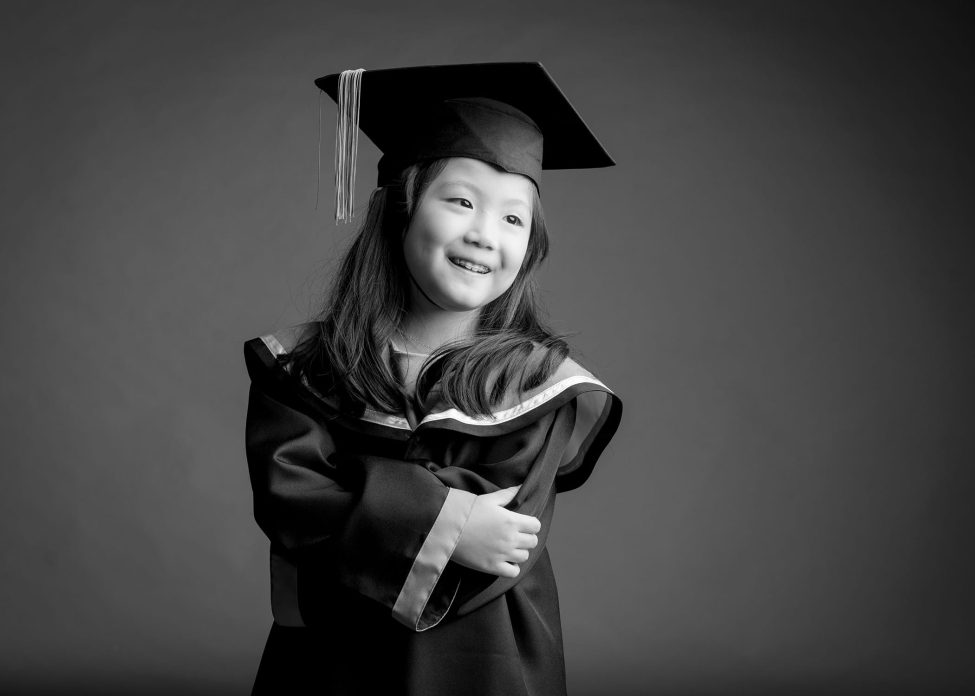 Black and white photo of girl in k2 kindergarten graduation gown and cap during a k2 kindergarten graduation photoshoot in Singapore Credit: White Room Studio