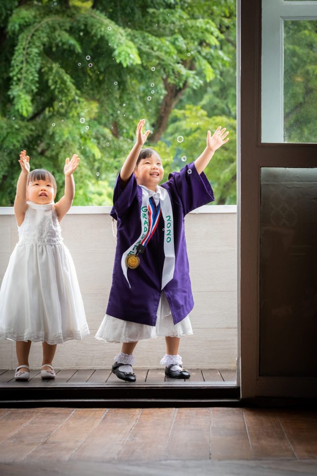 Girl in purple K2 kindergarten graduation gown and cap playing with bubbles with nature scenery background during a K2 kindergarten graduation photoshoot in Singapore Credit: White Room Studio