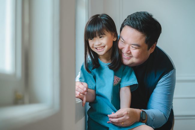 Father and daughter smiling in candid picture during k2 Kindergarten graduation family photoshoot in Singapore Credit: White Room Studio