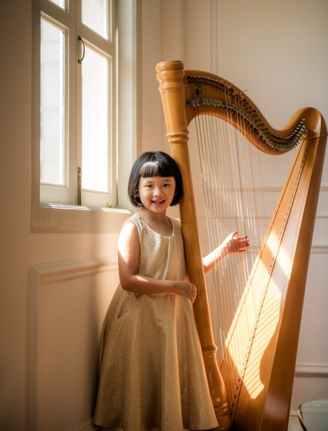 Young girl playing with harp near windows with natural light during a family photoshoot in Singapore Credit: White Room Studio