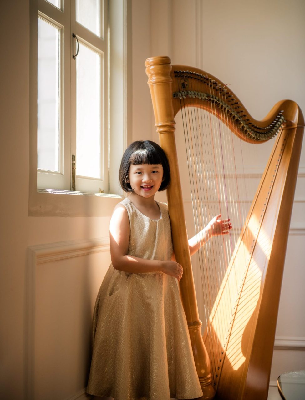 Young girl playing with harp near windows with natural light during a family photoshoot in Singapore Credit: White Room Studio