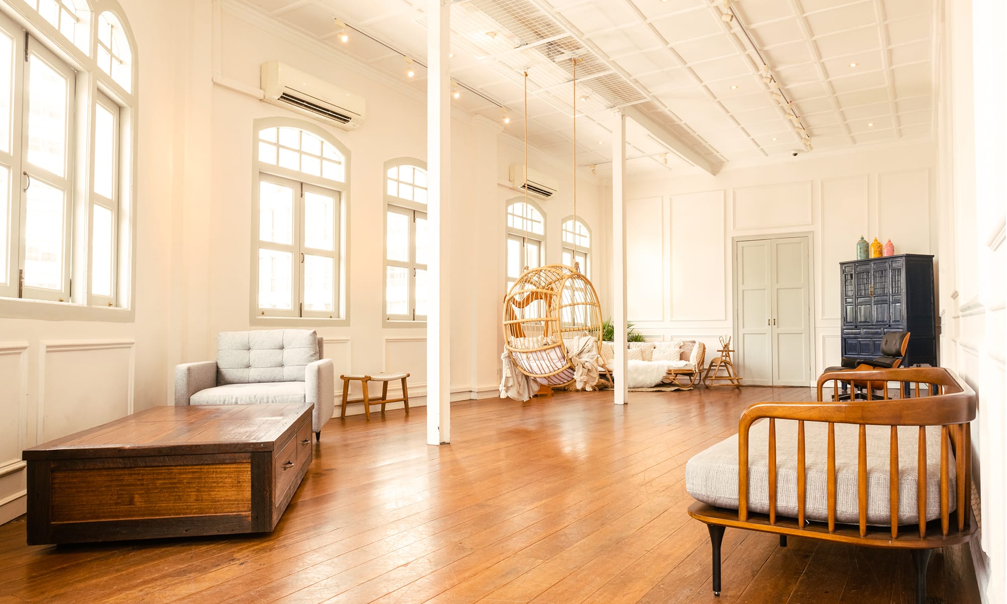Panoramic photo of a photography studio space with white walls with wainscoting, and tall windows with natural sunlight with rustic wooden furniture in River Valley, Singapore Credit: White Room Studio
