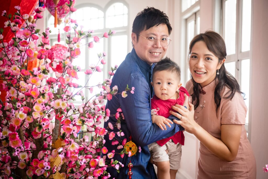 Mother and father hugging baby boy toddler during a Chinese New Year Family photoshoot with cherry blossoms decorations in Singapore Credit: White Room Studio