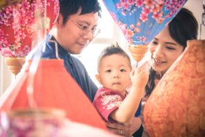 Mother and father hugging baby boy toddler during a Chinese New Year Family photoshoot with Chinese lanterns decorations in Singapore Credit: White Room Studio