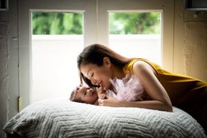 Mother smiling and look at newborn baby in a photography studio setting during a natural light newborn photoshoot in Singapore, White Room Studio. Credit: White Room Studio Pte Ltd