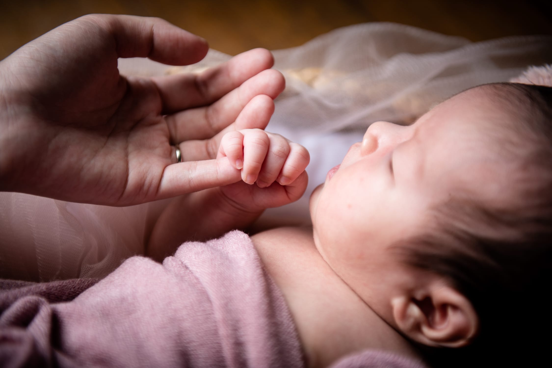 Sleeping newborn baby holding mother's hand in a photography studio setting during a natural light newborn photoshoot in Singapore, White Room Studio. Credit: White Room Studio Pte Ltd