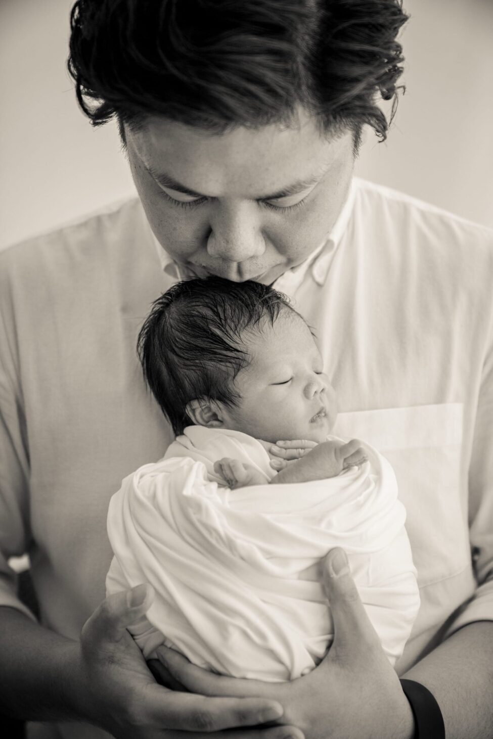 Father carrying their newborn baby in a photography studio setting during a newborn photoshoot in Singapore, White Room Studio. Credit: White Room Studio Pte Ltd