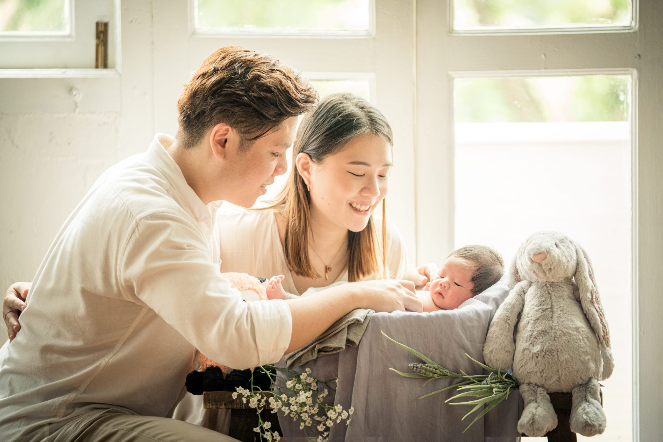 Family with parents and their newborn baby in a photography studio setting during a newborn photoshoot in Singapore, White Room Studio. Credit: White Room Studio Pte Ltd