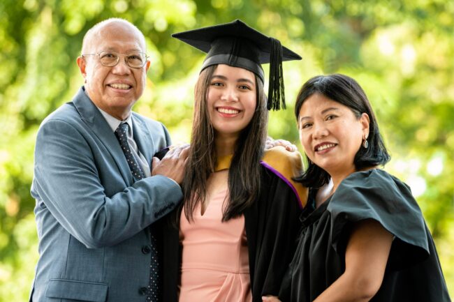 Professional Graduation & Family Photoshoot in Photography Studio, Singapore Family with parents and their children wearing a graduation gown and cap within a photography studio setting during a graduation photoshoot in Singapore, White Room Studio. Credit: White Room Studio Pte Ltd