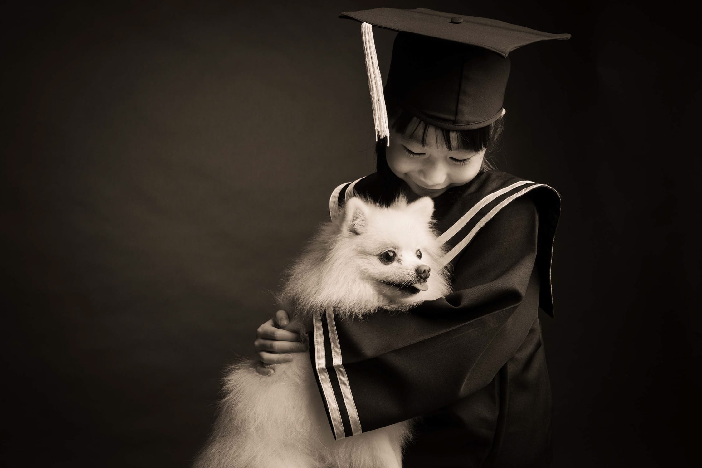 Girl in K2 kindergarten graduation gown and cap with her pet dog during a k2 kindergarten graduation photoshoot in Singapore Credit: White Room Studio