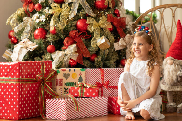 Smiling girl with Christmas tree and Christmas presents in a photography studio setting during a Christmas family photoshoot in Singapore, White Room Studio. Credit: White Room Studio Pte Ltd