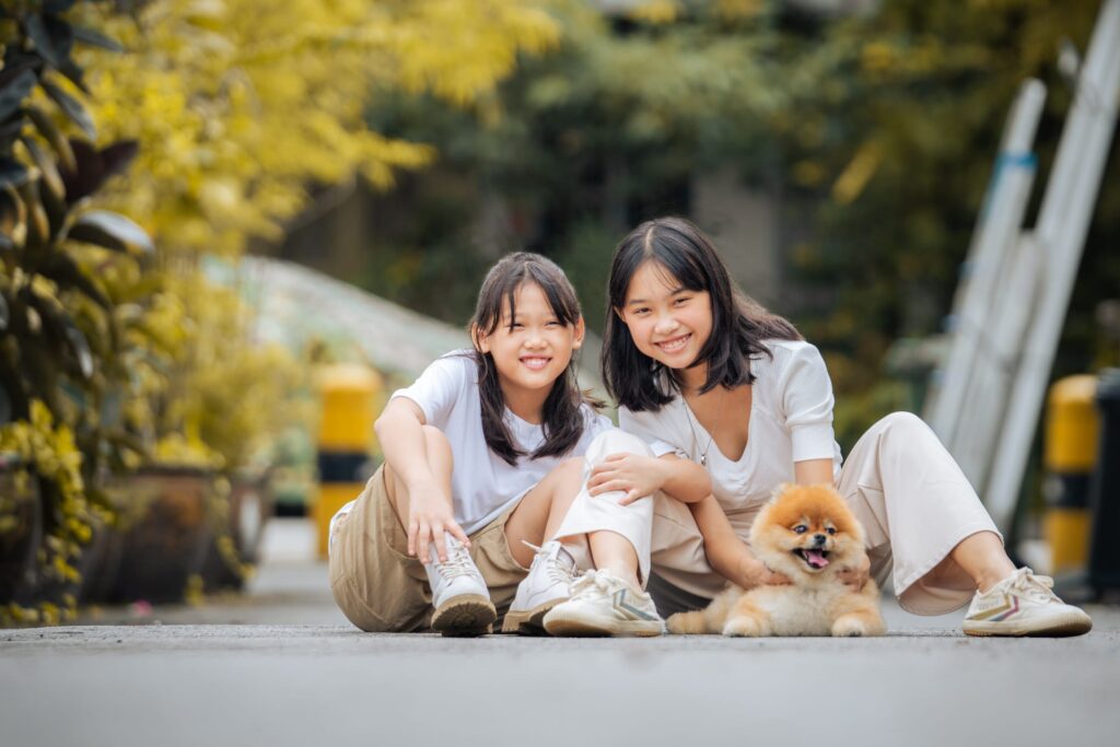 Two siblings (sisters) with their pet dog in an outdoor setting during an outdoor family photoshoot in Singapore, Tiong Bahru. Credit: White Room Studio Pte Ltd