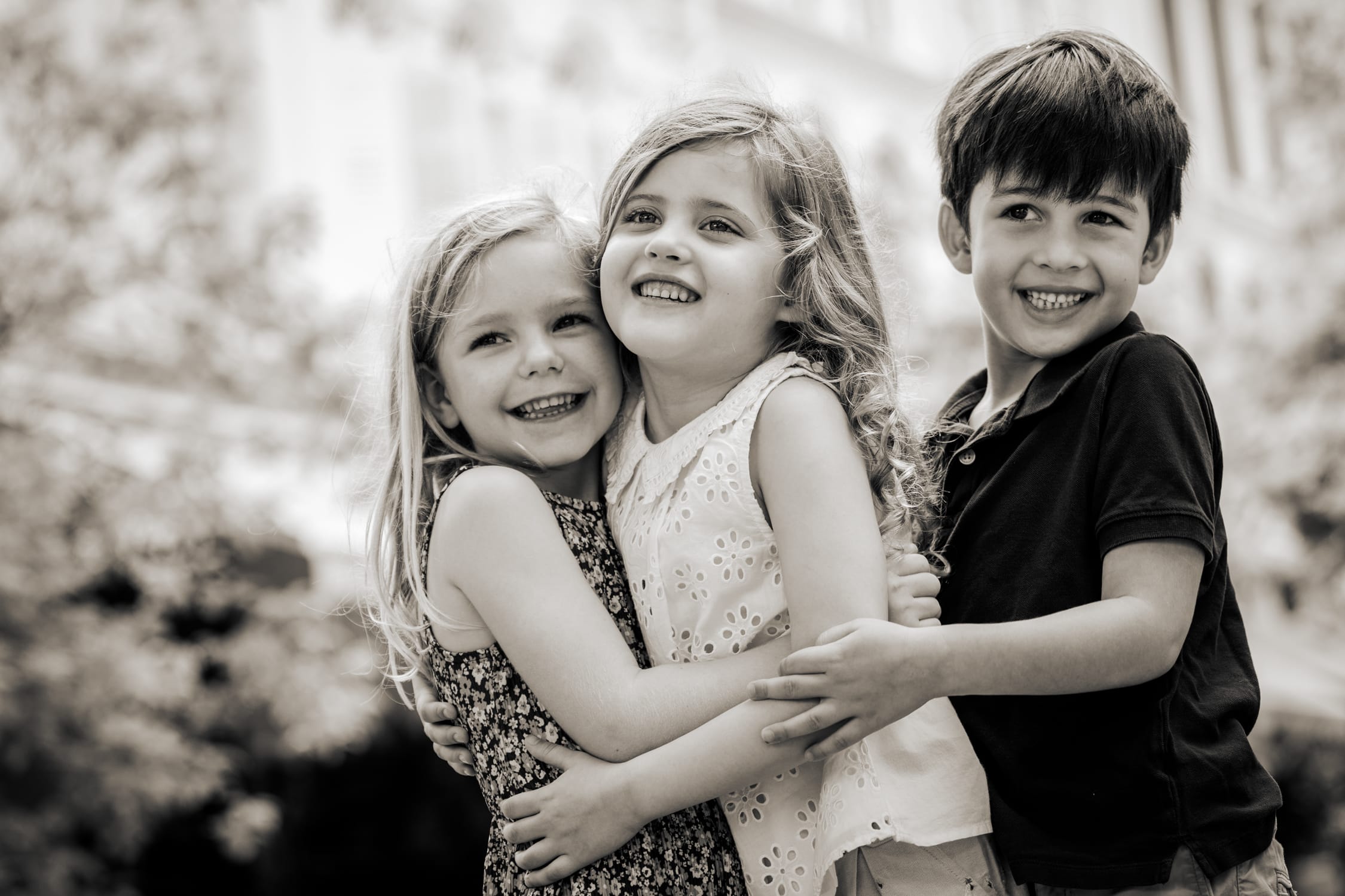 Professional Family & Multi Generation Photoshoot in Photography Studio, Singapore Three children smiling and hugging each other in an outdoor setting during an outdoor family photoshoot in Singapore, White Room Studio. Credit: White Room Studio Pte Ltd