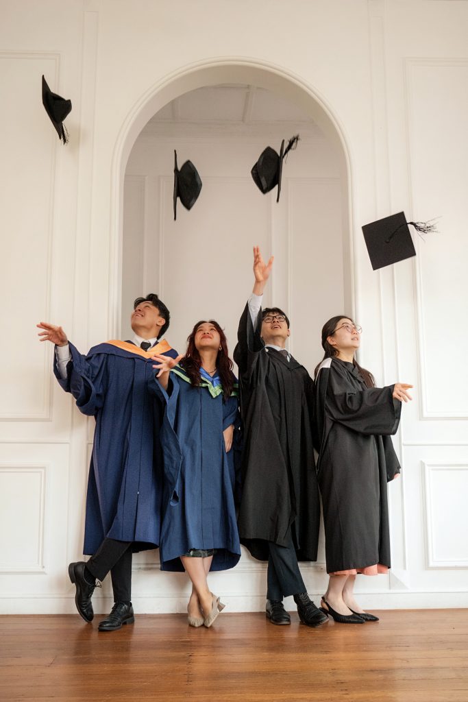 Graduates in graduation gowns and throwing their mortarboards in a photography studio setting during a family photoshoot in Singapore, White Room Studio. Credit: White Room Studio Pte Ltd