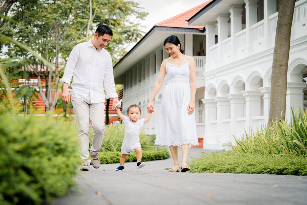 Family with mother and father holding toddler son's hands during an outdoor family photoshoot in Capella Hotel Singapore. Credit: White Room Studio Pte Ltd