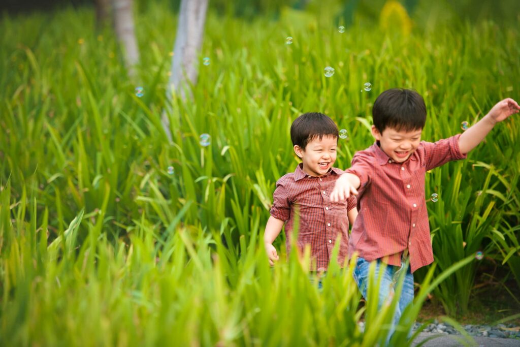 Two young boys playing in a grass field during an outdoor family photoshoot in Singapore, Capella Hotel. Credit: White Room Studio Pte Ltd