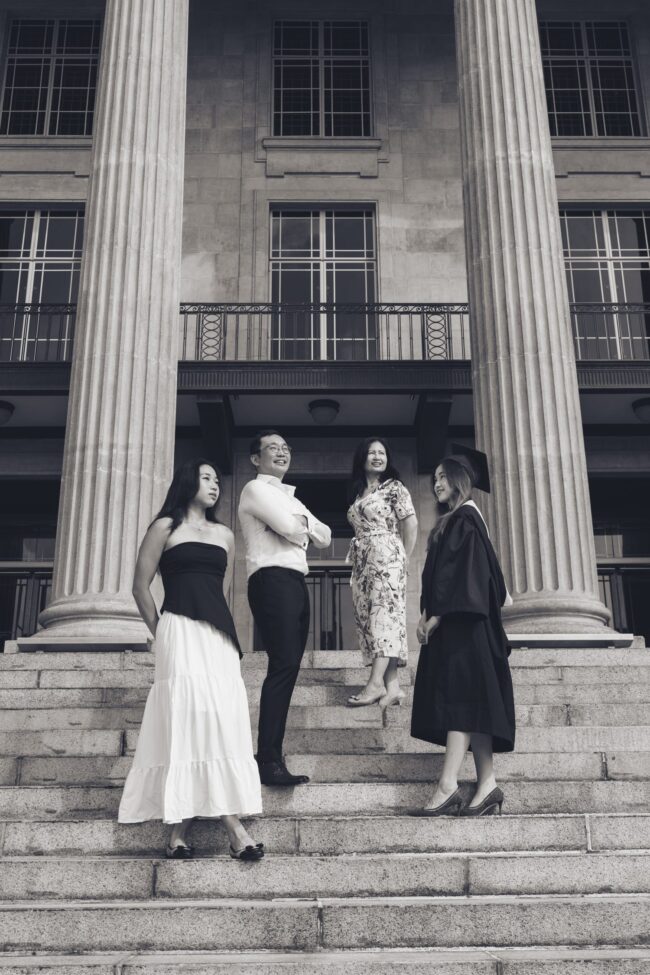 Family with mother and father and two daughters (one in graduation gown) during an outdoor graduation photoshoot in National Gallery Singapore. Credit: White Room Studio Pte Ltd