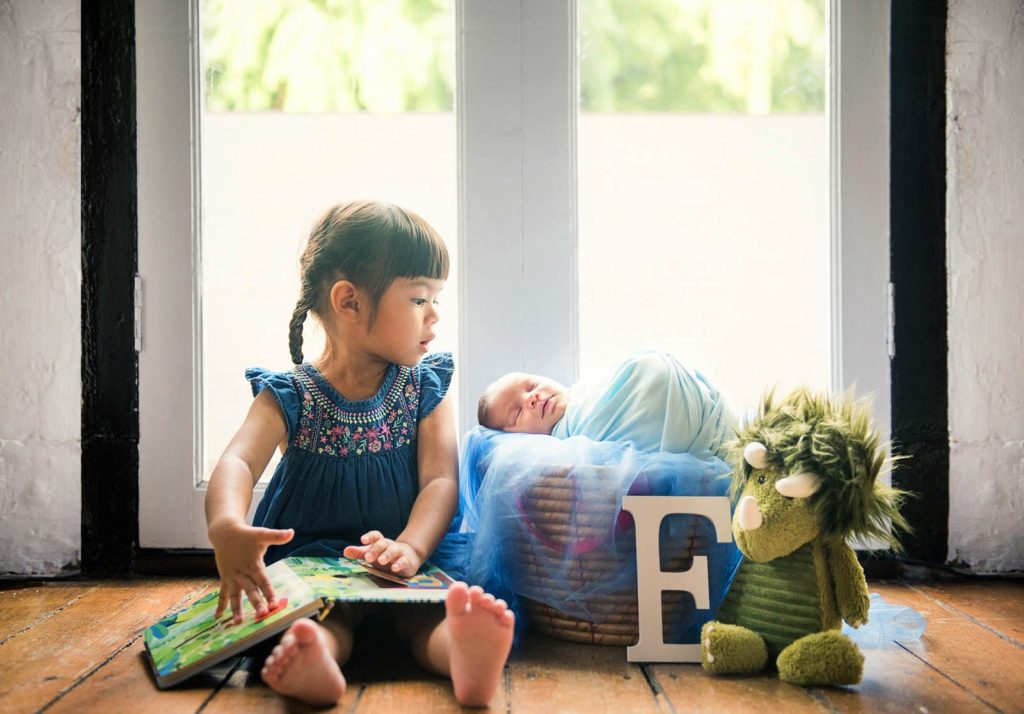 Elder sister looking at her newborn sibling during a family newborn photoshoot at White Room Studio, Singapore