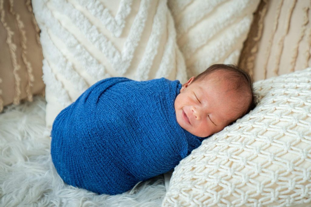 Sleeping newborn wrapped in blue on a knitted blanket at White Room Studio Singapore