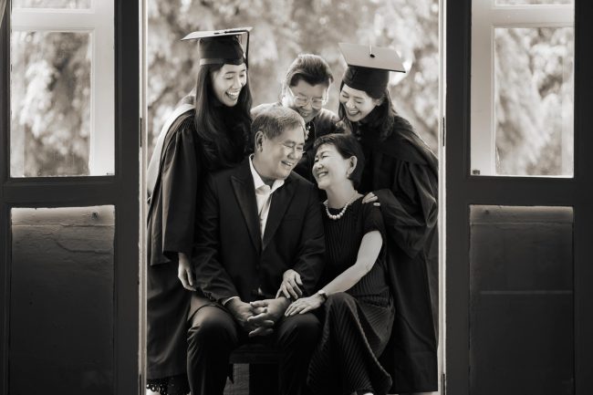 Graduates in graduation gowns and throwing their mortarboards in a photography studio setting during a family photoshoot in Singapore, White Room Studio. Credit: White Room Studio Pte Ltd